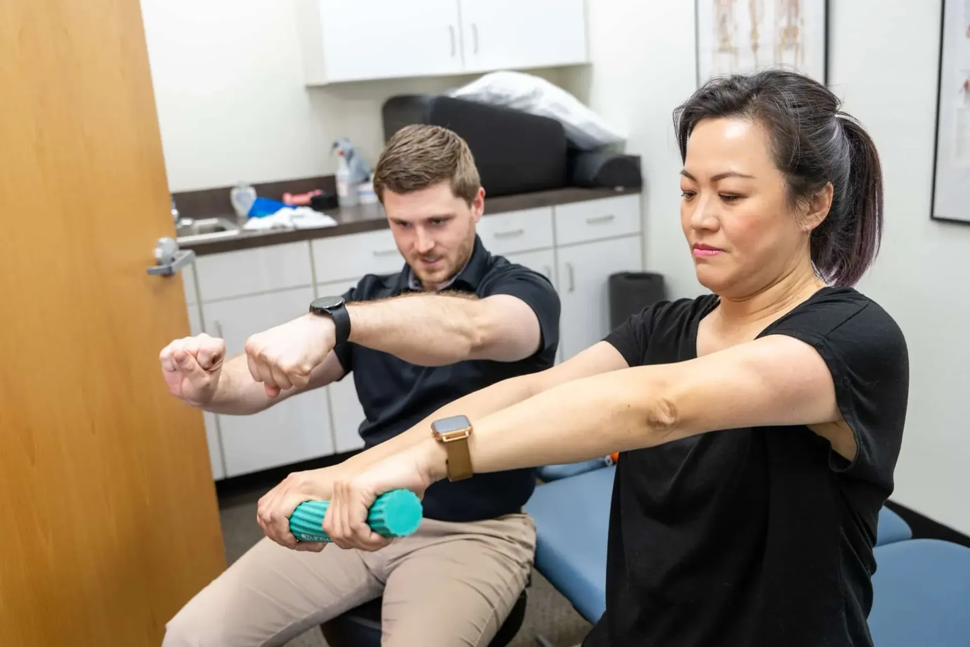 Two people doing seated arm stretches in an office, wearing wrist weights.