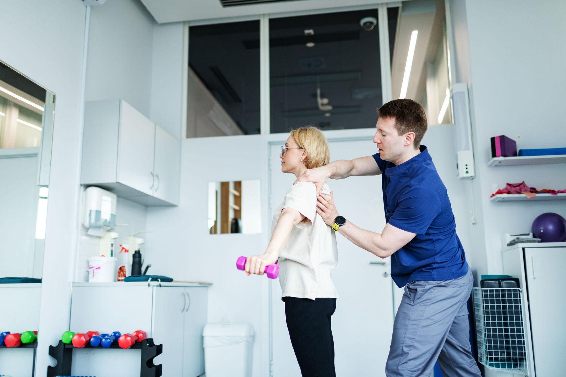 Two people in a bright kitchen, one adjusting the other's shirt collar near a sink and cabinets