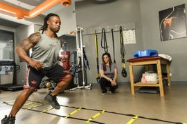 Athlete doing agility drills in a gym while a coach watches in the background