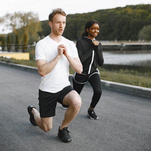 Two people doing a lunge workout on a road outdoors, wearing athletic clothes.