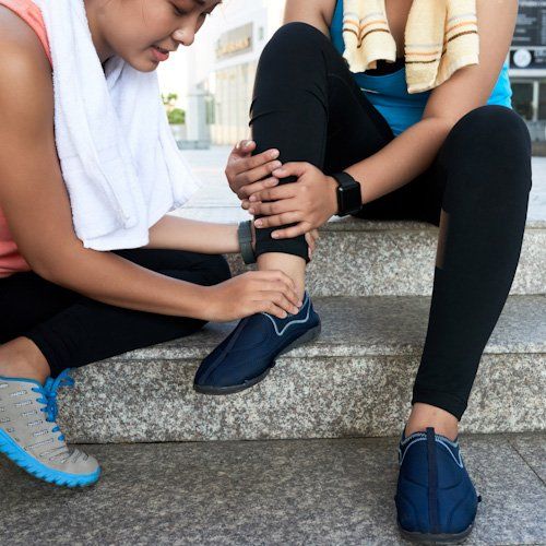 Person adjusting another person's ankle on outdoor steps after an injury, with a shoe nearby
