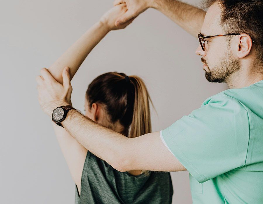 Two people stretching together, one assisting the other in a mint green shirt indoors