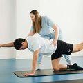 Physical therapy session with a trainer assisting a person on all fours doing a balancing stretch on a mat