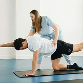 Physical therapist helping a man do a tabletop stretch on a yoga mat in a bright room