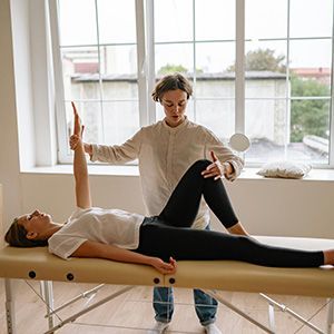 Physical therapist assisting a woman with leg stretch on a treatment table in a bright studio