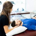 Therapist gently supports a patient's head during a treatment session on a clinic table