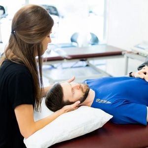 Therapist gently supports a patient's head during a treatment session on a clinic table