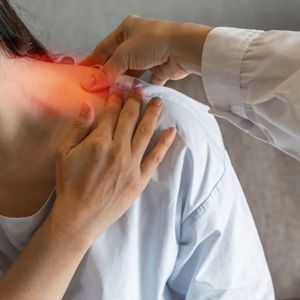 Doctor examining a patient’s neck and shoulder with red pain highlight