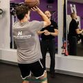 Athlete shooting a basketball indoors while a trainer watches in a gym mirror.