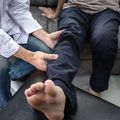 Person in dark pants has a bare foot examined by a clinician in a white coat.