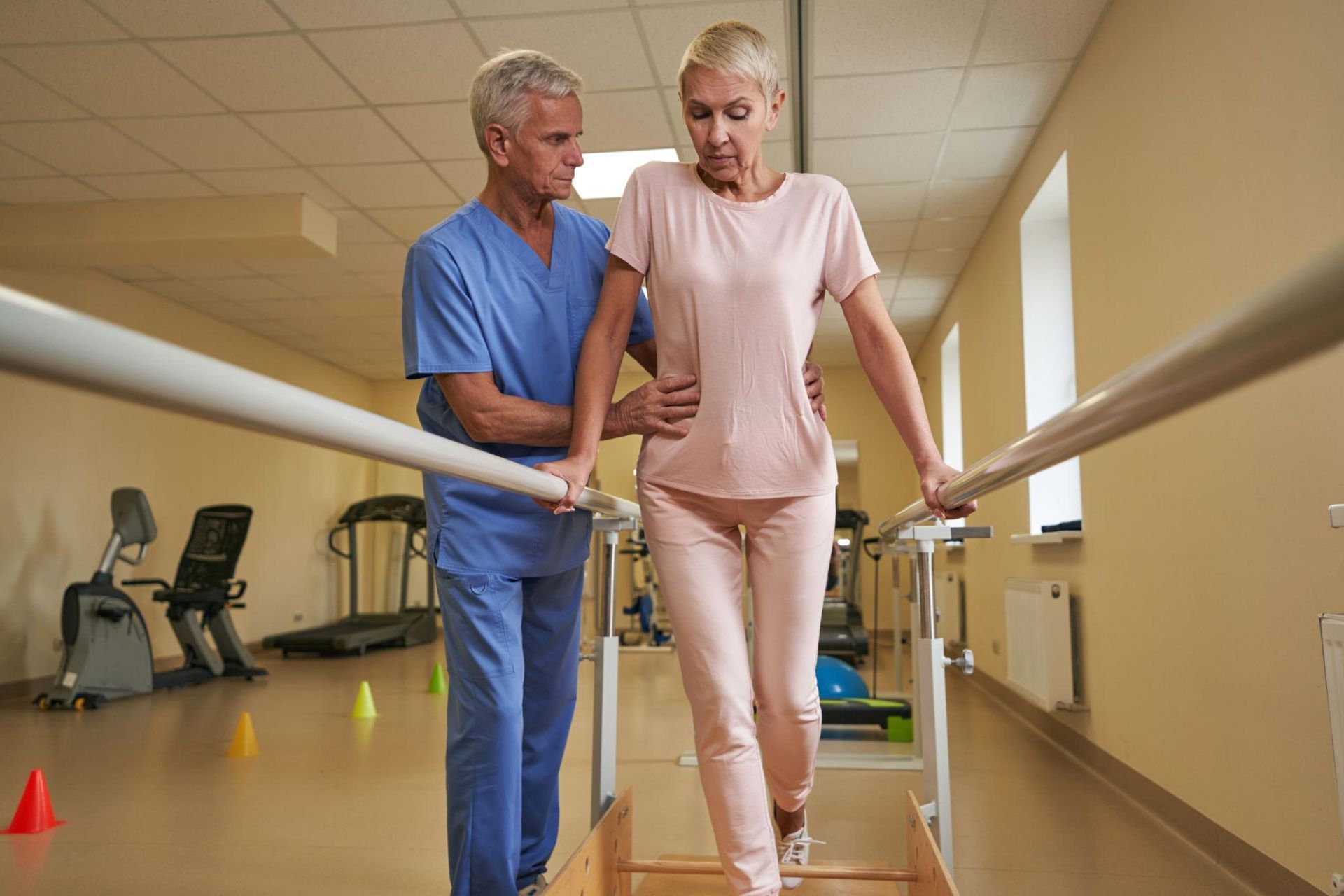 Physical therapist assisting patient walking on parallel bars in a rehab gym