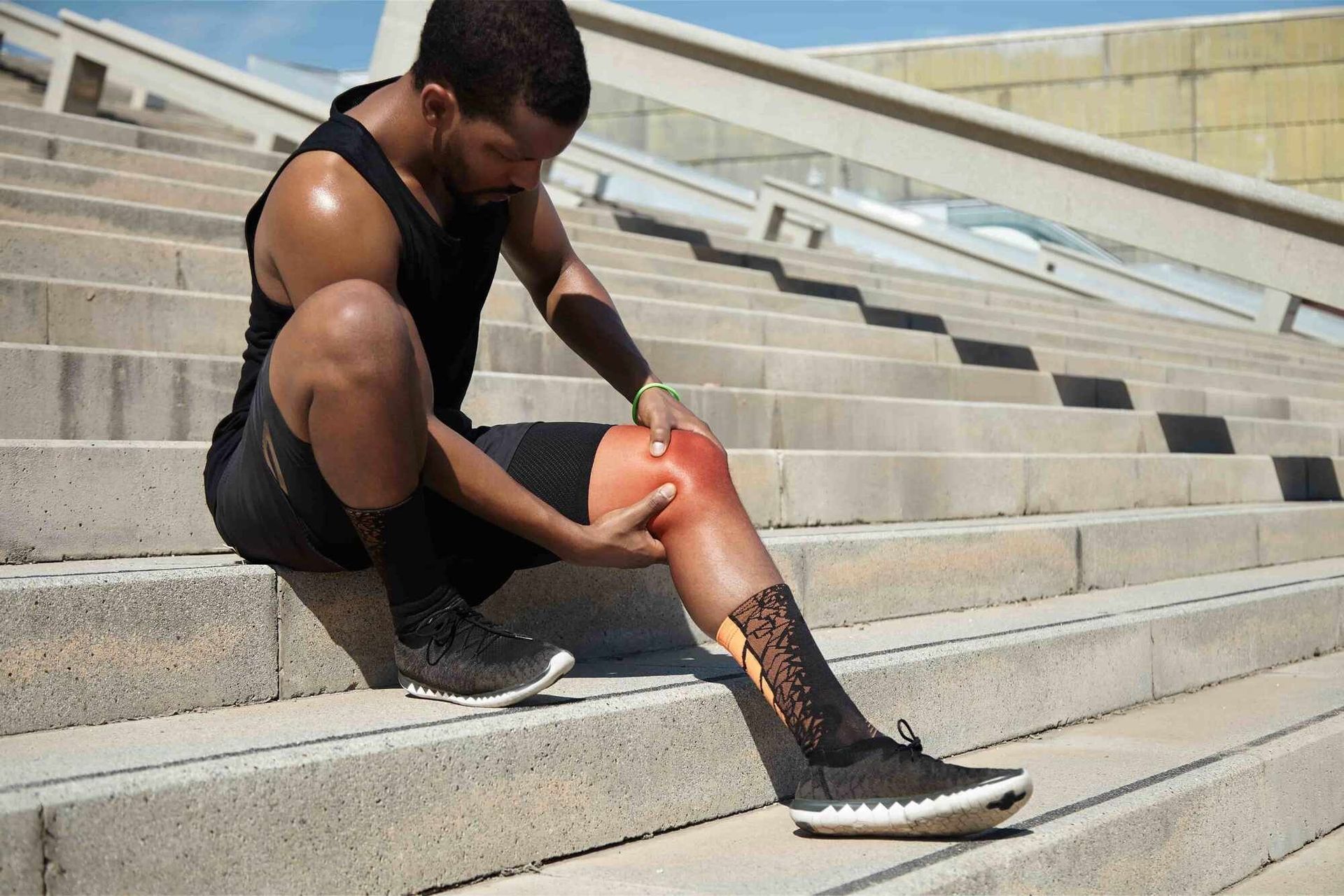 Person sitting on outdoor steps, holding a red knee, with a leg wound and black sneakers.
