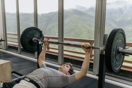 Person bench pressing a barbell in a gym with large windows and mountain views