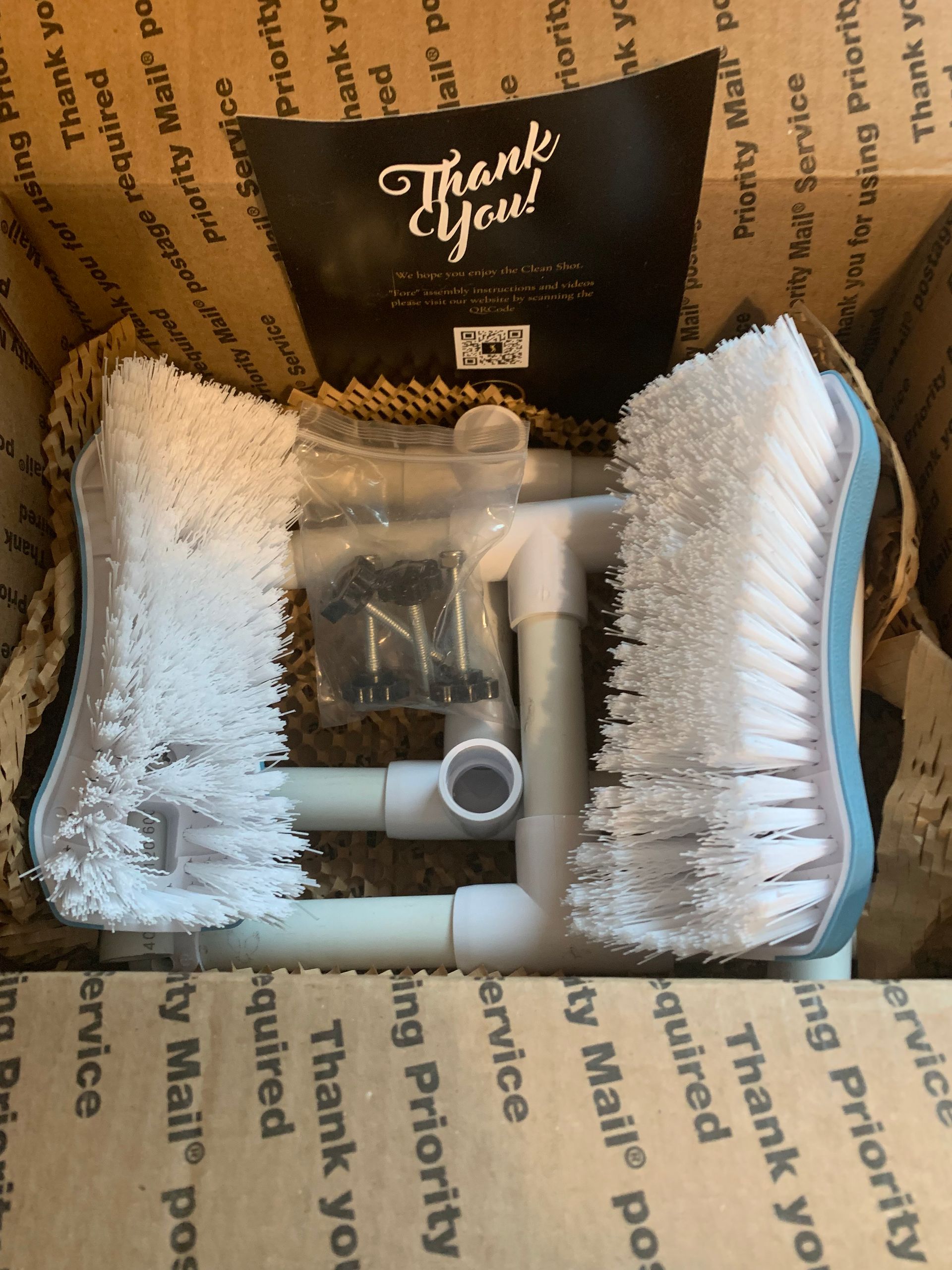 Box with a white PVC pipe assembly and two white scrub brushes. A 