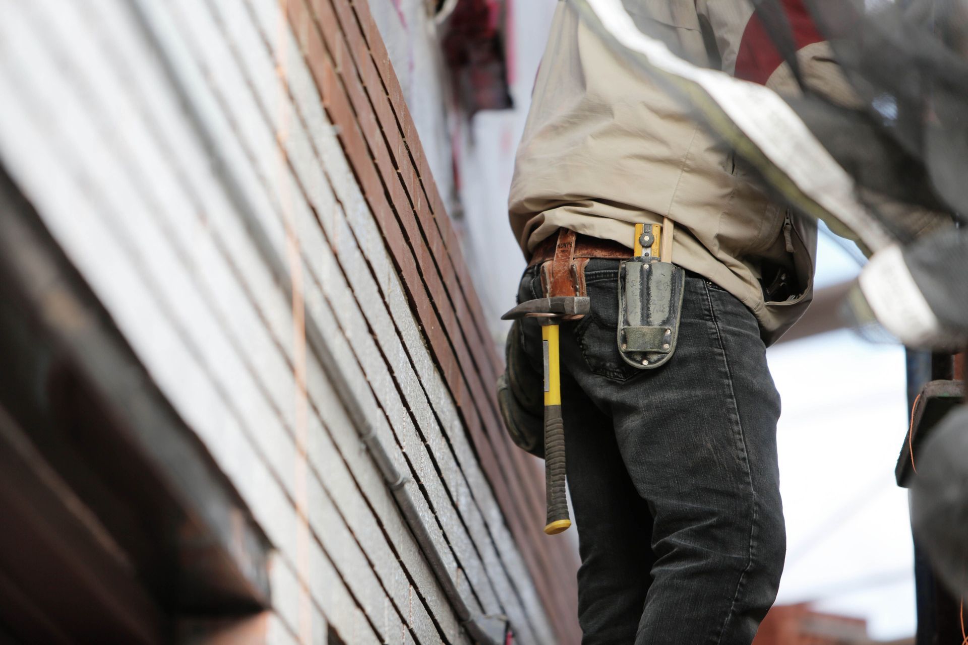 Handyman with tool belt standing beside a metal wall, holding a yellow level tool.