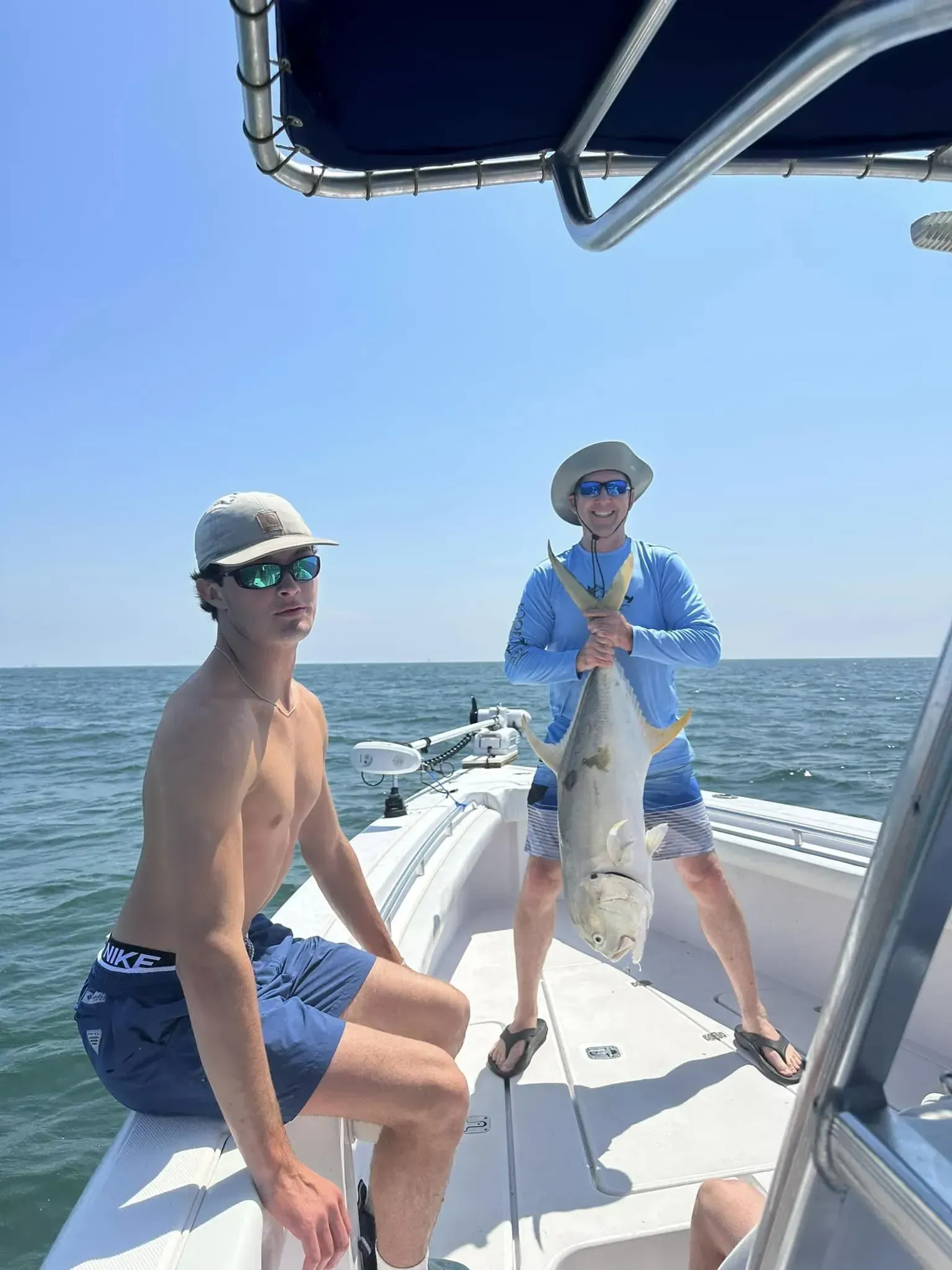 Two men are sitting on a boat holding a large fish.