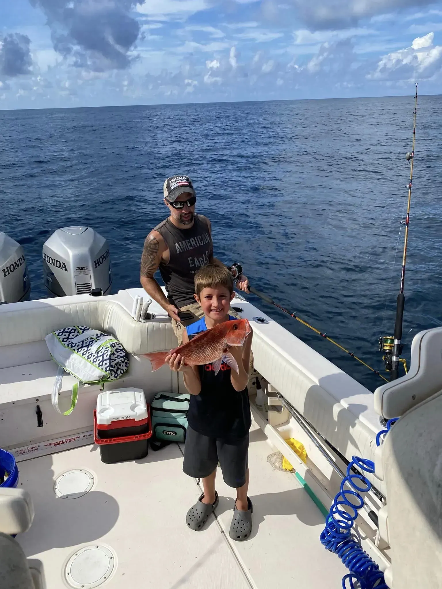 A man and a boy are standing on a boat holding a fish.