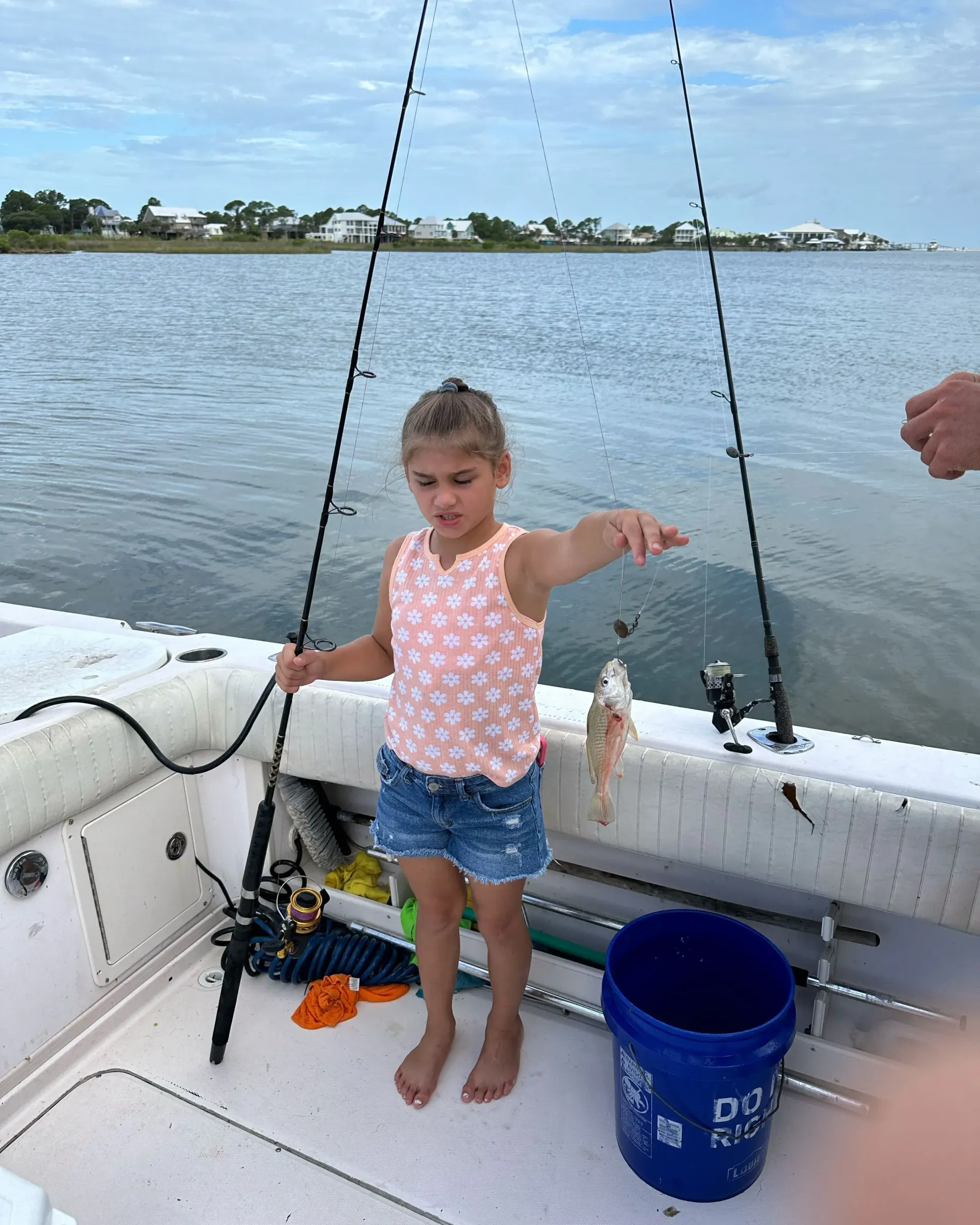 A little girl is standing on a boat holding a fishing rod and a fish.