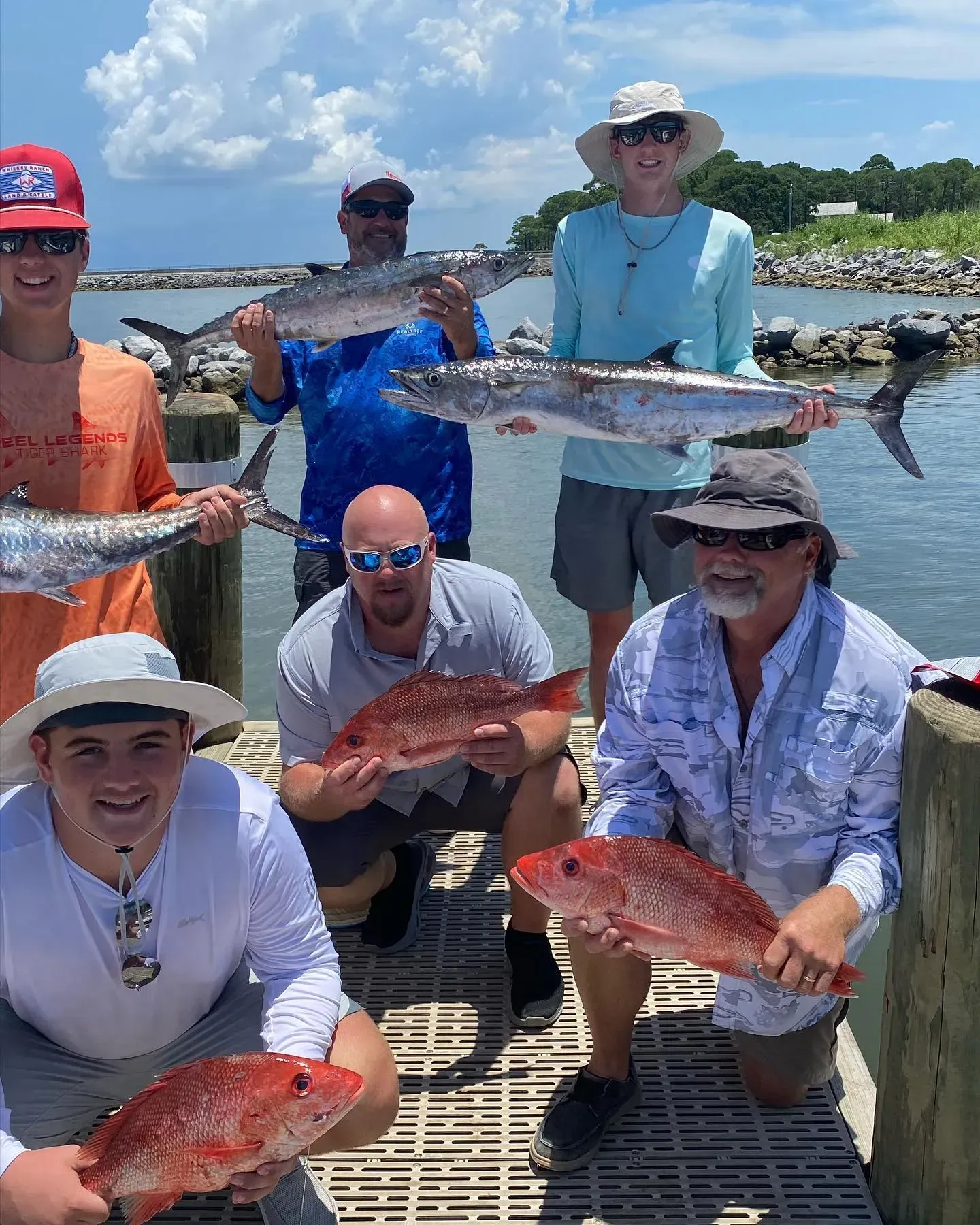 A group of men are holding fish on a dock.