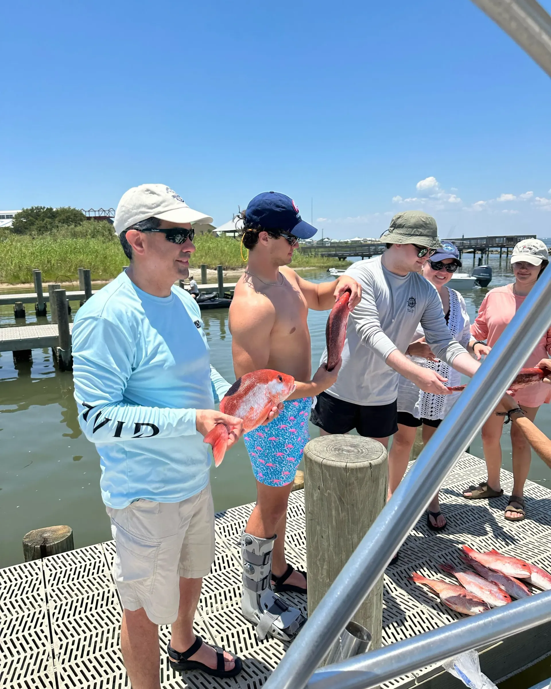 A group of people are standing on a dock holding fish.