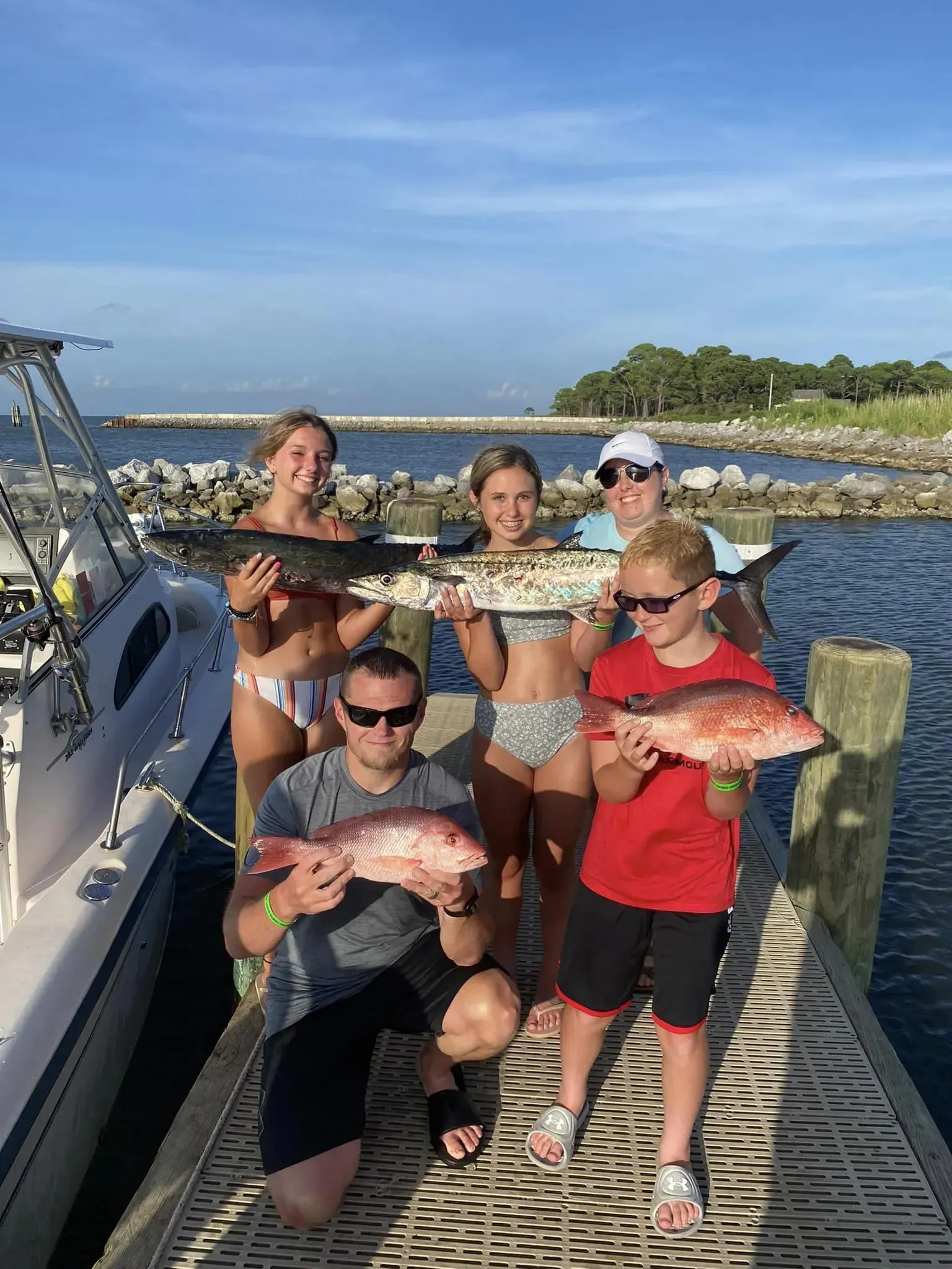 A group of people are standing on a dock holding fish.