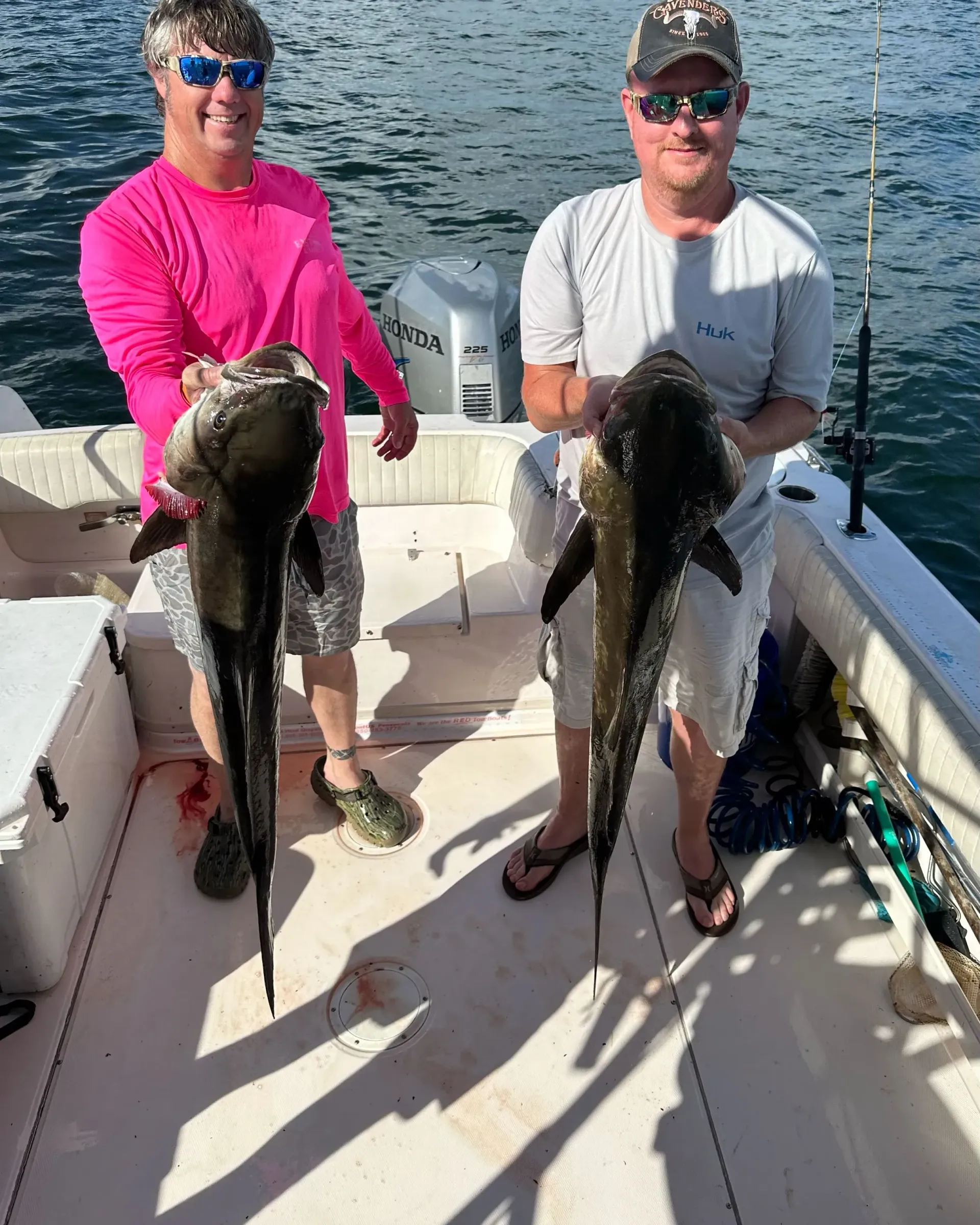 Two men are standing on a boat holding fish.