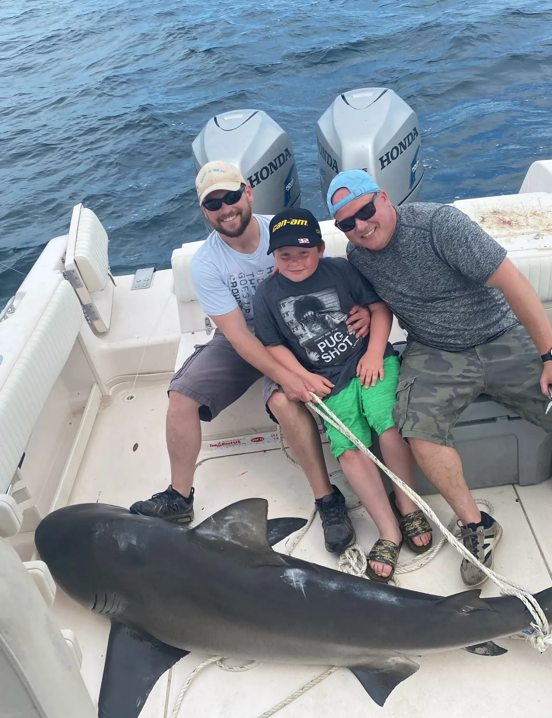 Three men and a boy are sitting on a boat next to a shark.
