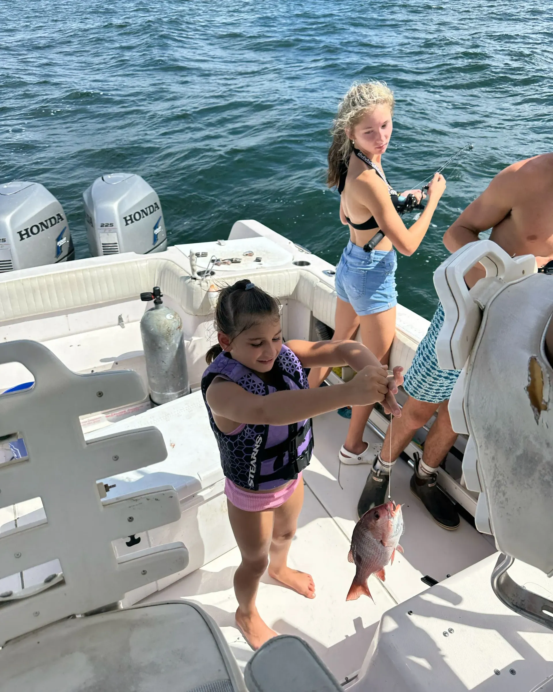 A man and two girls are fishing on a boat.