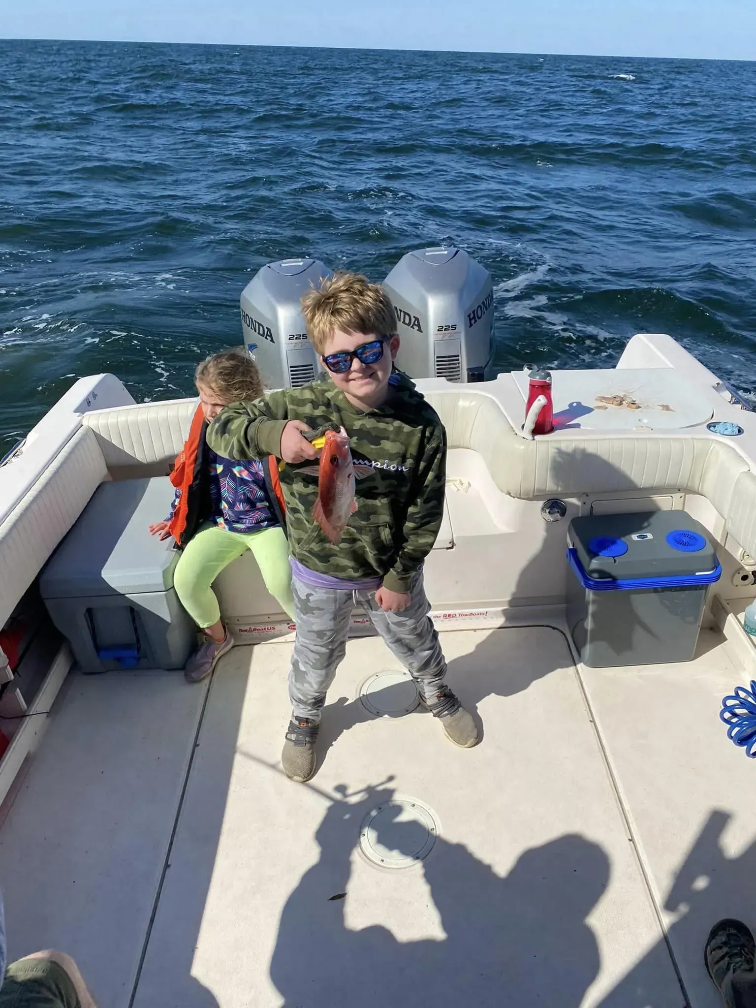 A boy and a girl are fishing on a boat in the ocean.