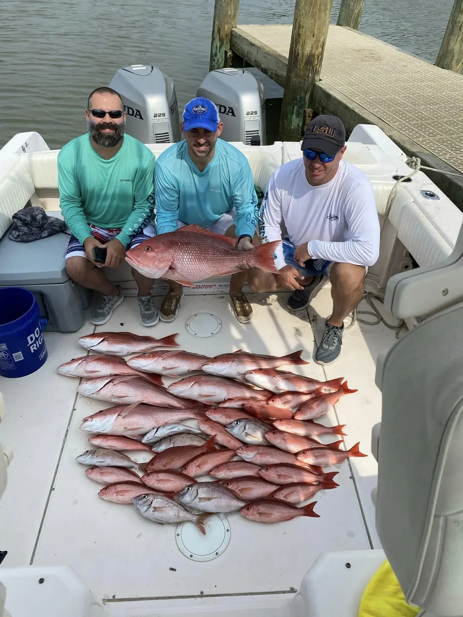 Three men are sitting on a boat holding a large fish.