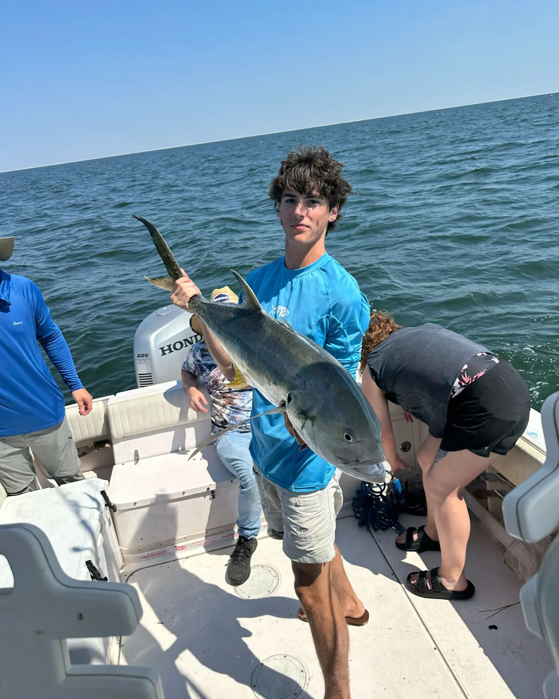 A young man is holding a large fish on a boat.