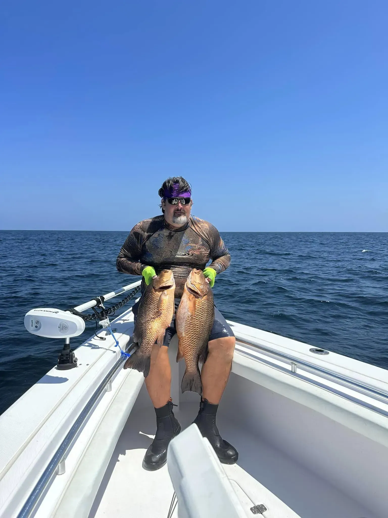 A man is sitting on a boat holding two fish.
