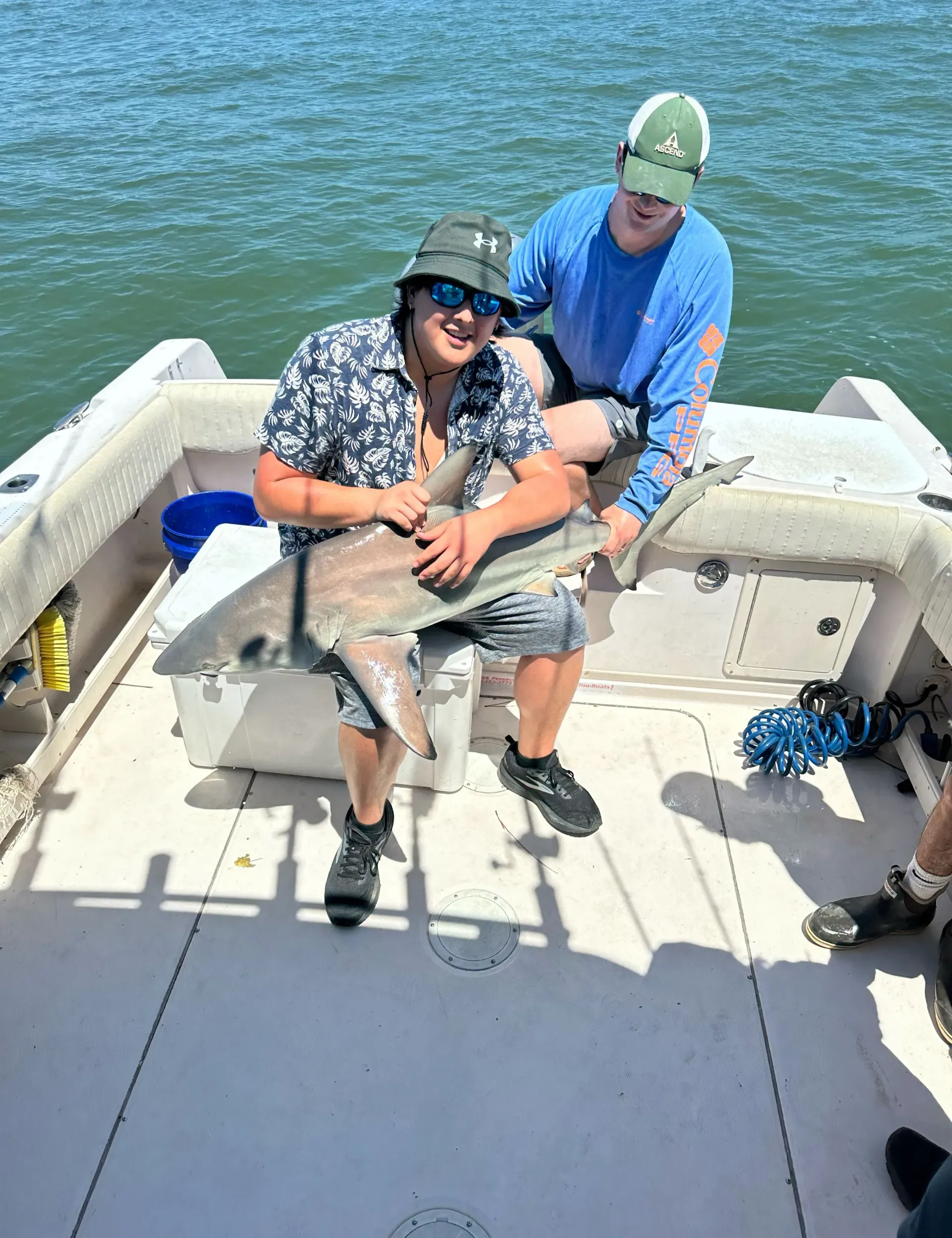 Two men are sitting on a boat holding a large fish.