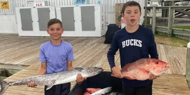 Two young boys are holding large fish on a dock.