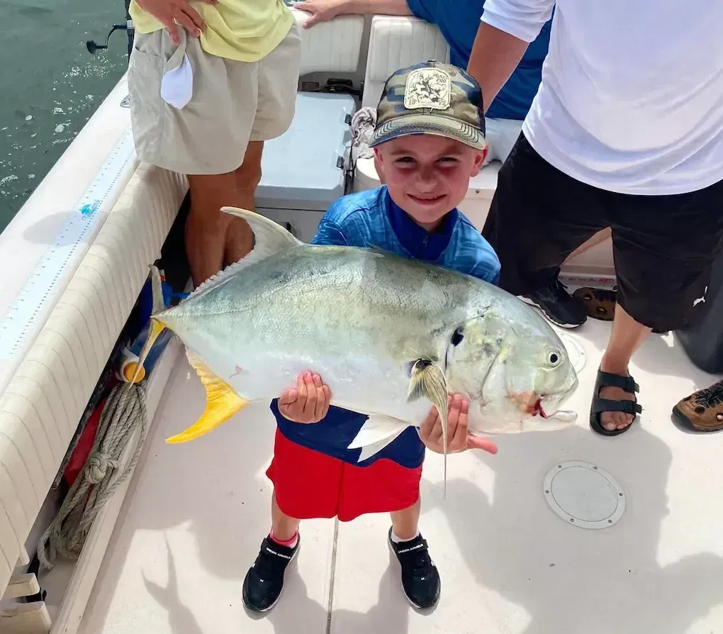 A young boy is holding a large fish on a boat