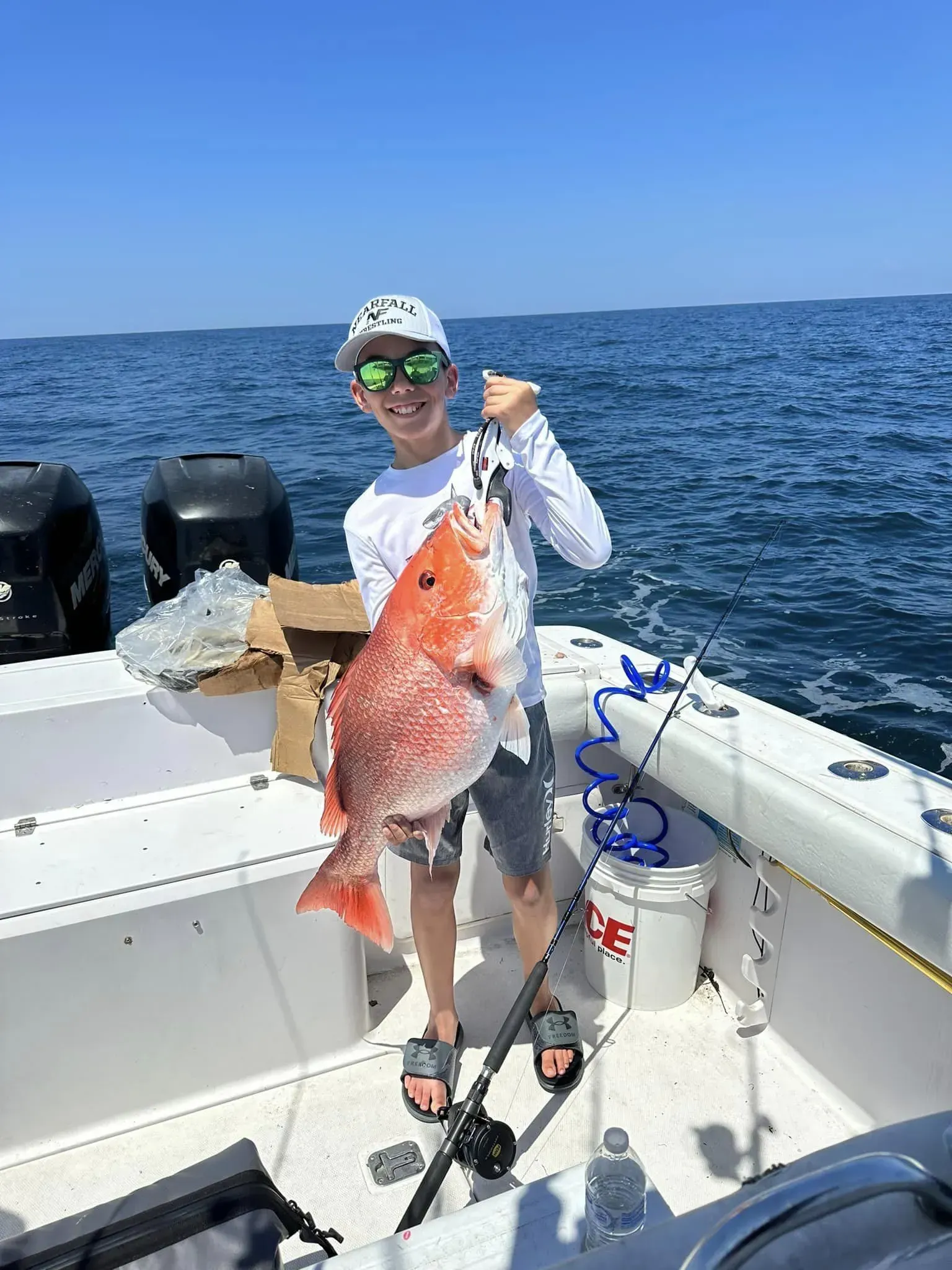 A young man is holding a large red fish on a boat.
