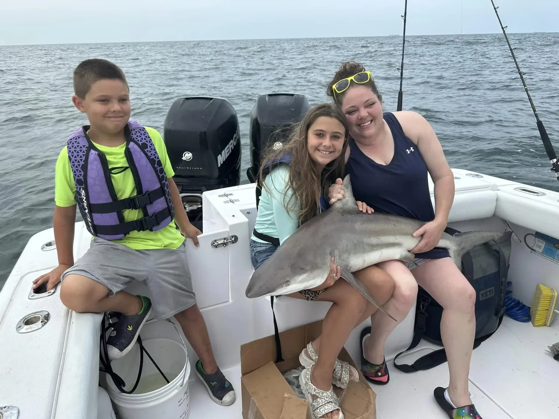 A group of people are sitting on a boat holding a shark.