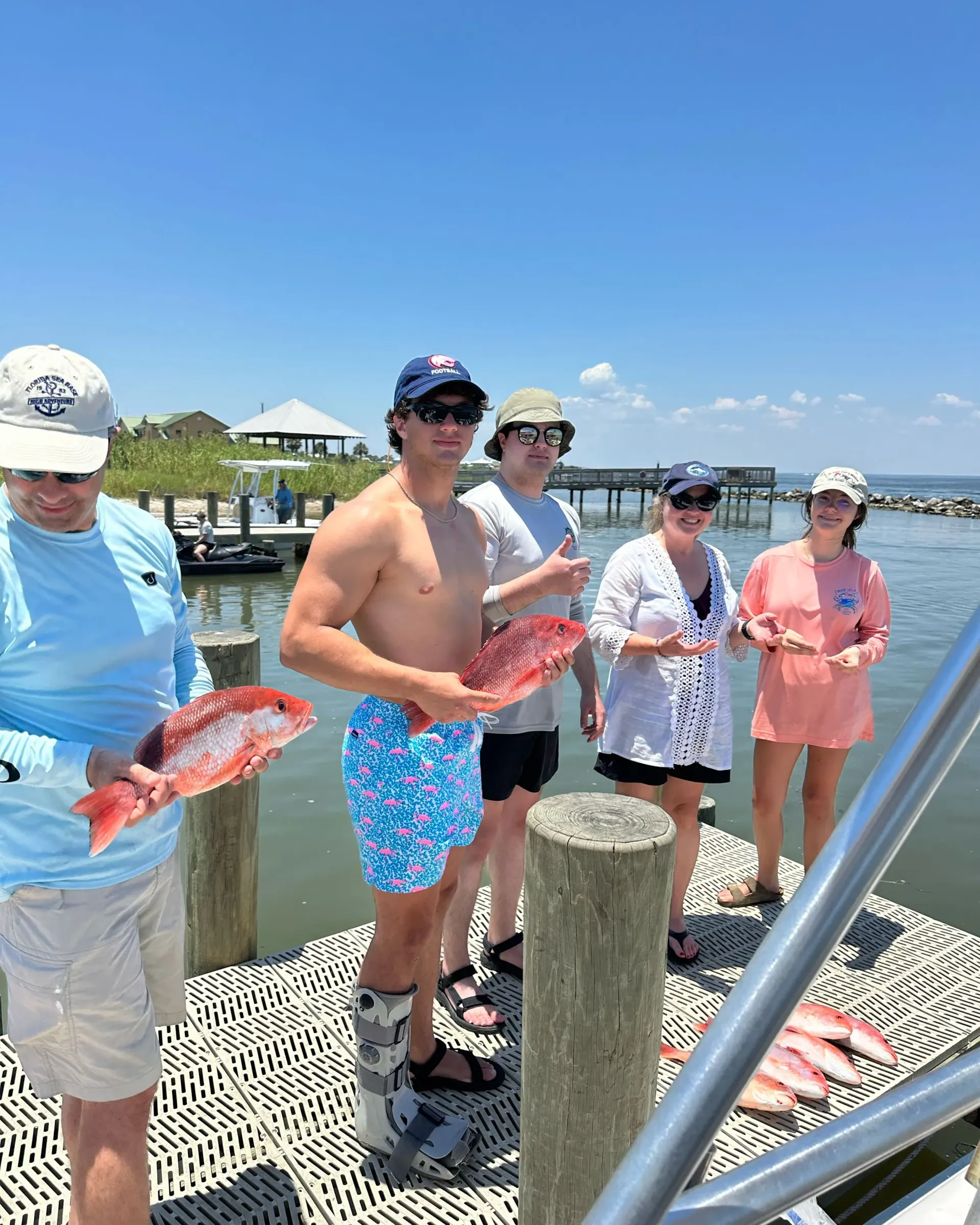 A group of people are standing on a dock holding fish.