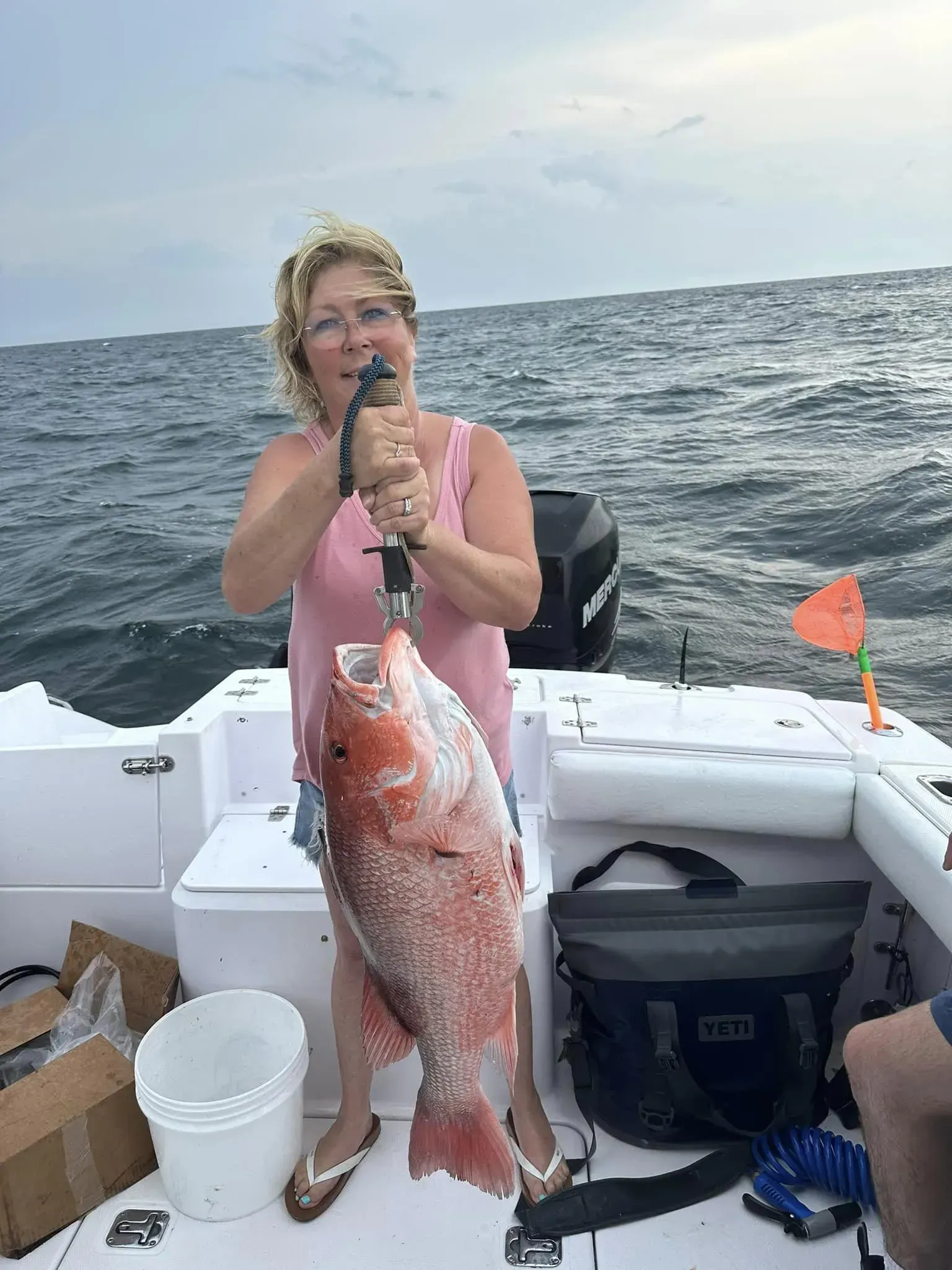 A woman is holding a large red fish on a boat in the ocean.