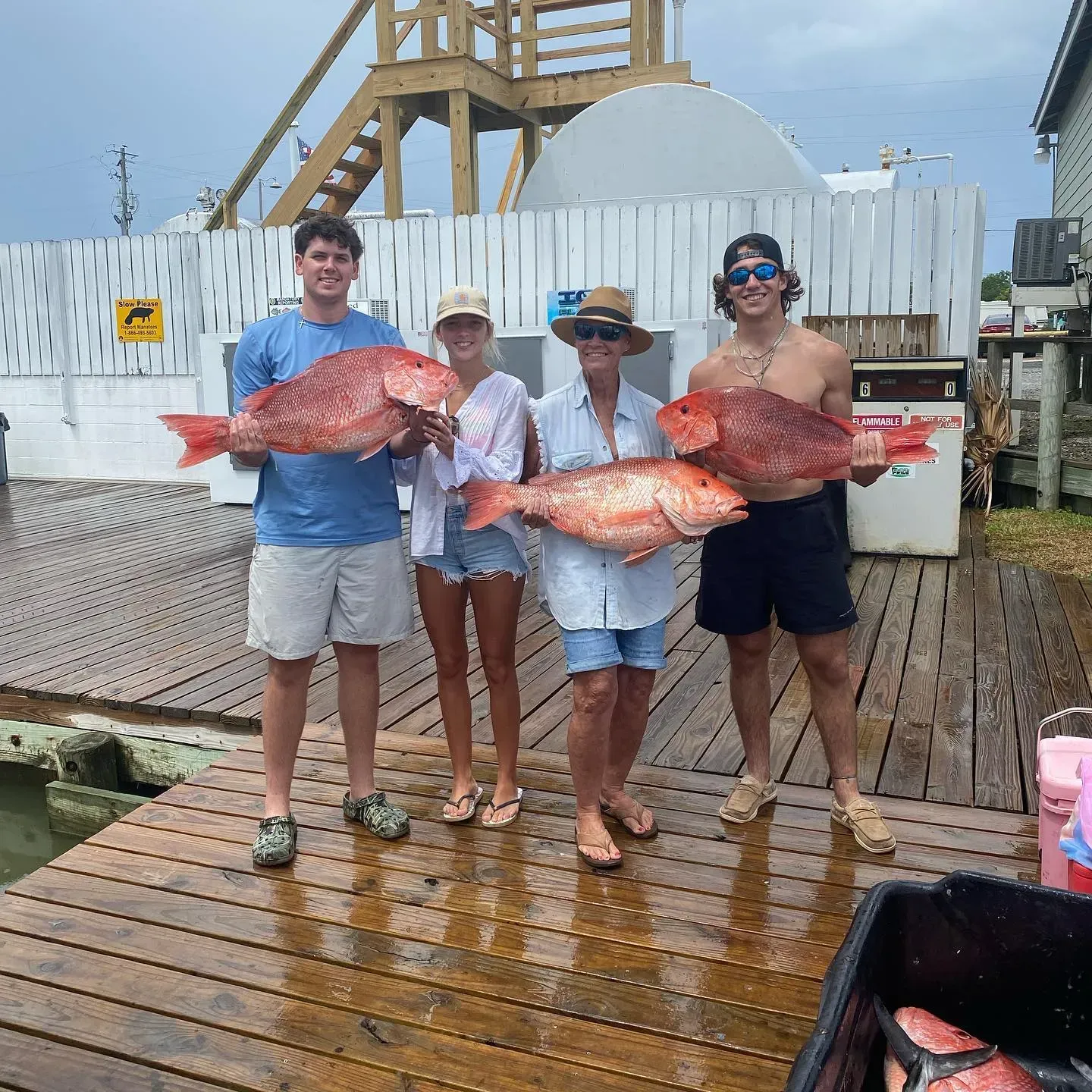 A group of people are standing on a dock holding large fish.