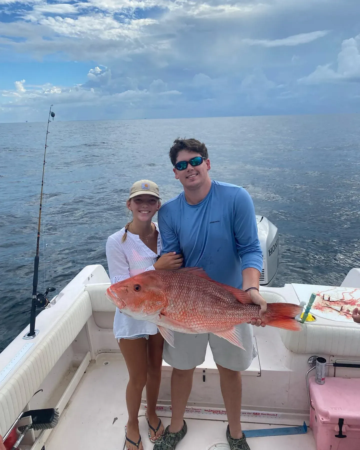 A man and a woman are standing on a boat holding a large red fish.
