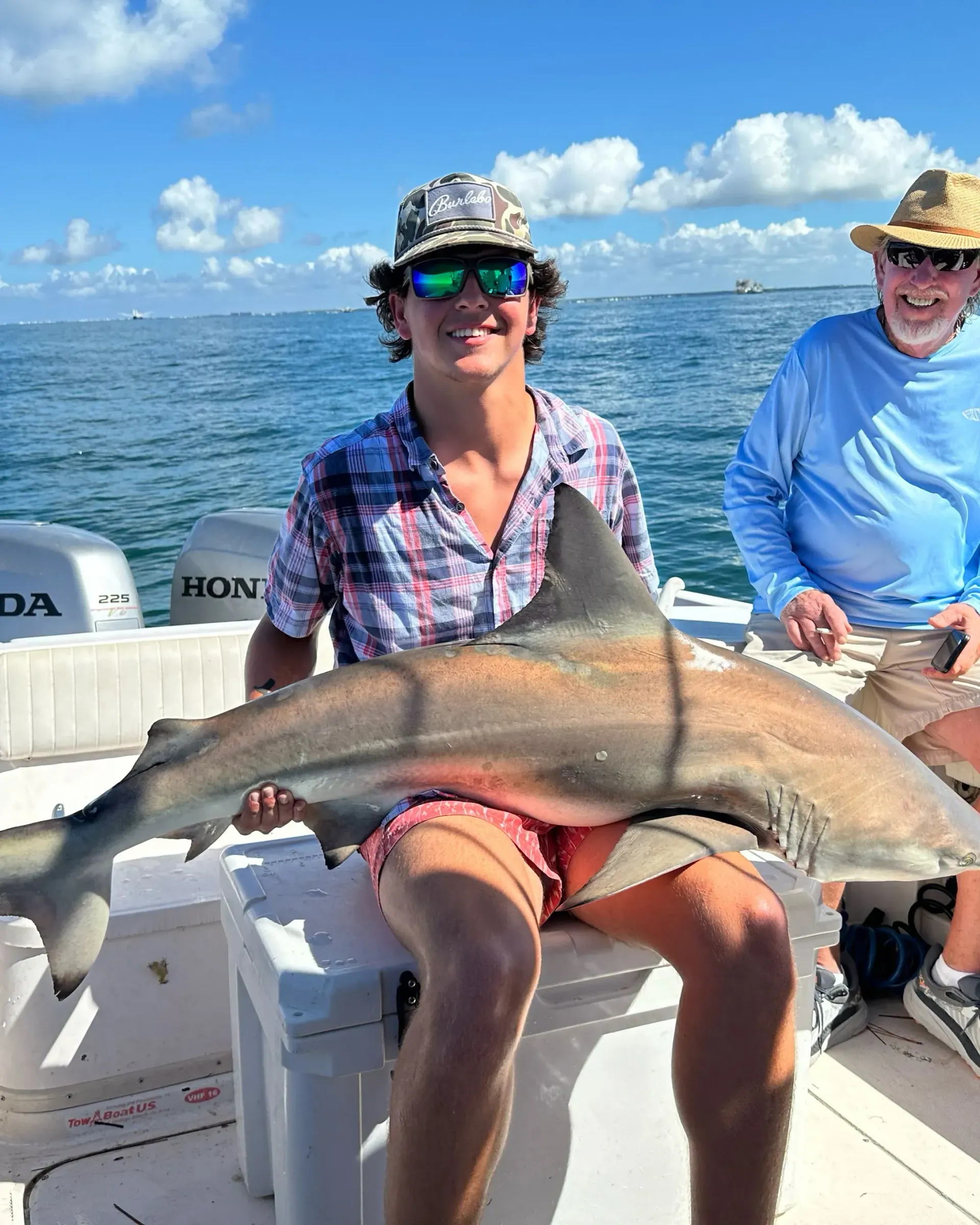 A man is sitting on a boat holding a large shark.
