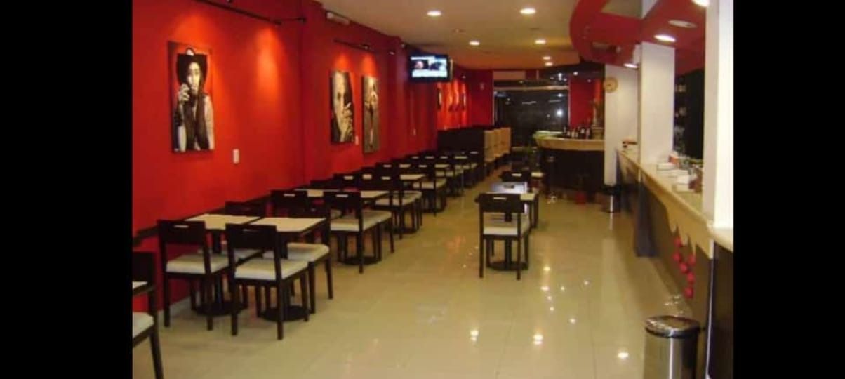 Interior de un restaurante de paredes rojas con filas de mesas y sillas; un bar al fondo.