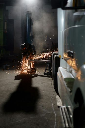 A man is welding a piece of metal in a garage at night.