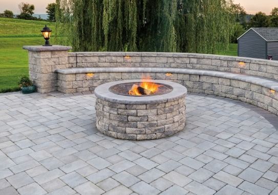 A fire pit is sitting on top of a brick patio next to a stone wall.