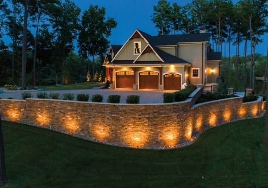 A large house is lit up at night with a stone wall surrounding it