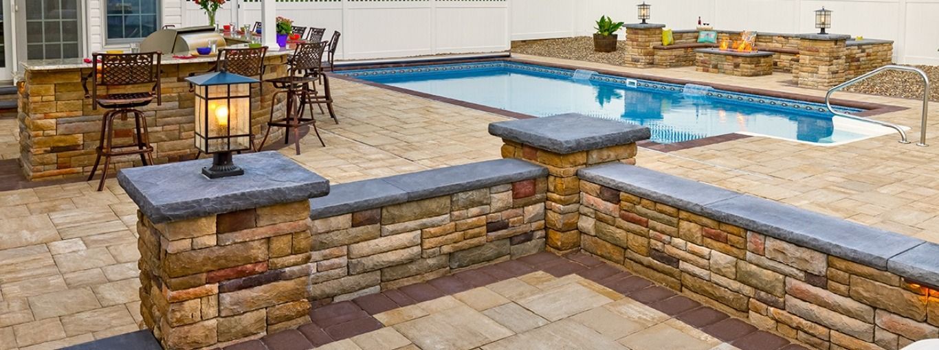 A large swimming pool is surrounded by a stone wall and patio.