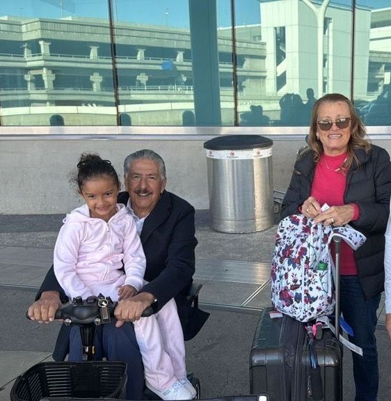 A little girl is sitting on a scooter next to a man and woman
