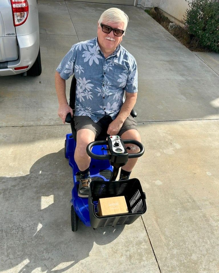 A man is sitting on a blue scooter in a driveway.