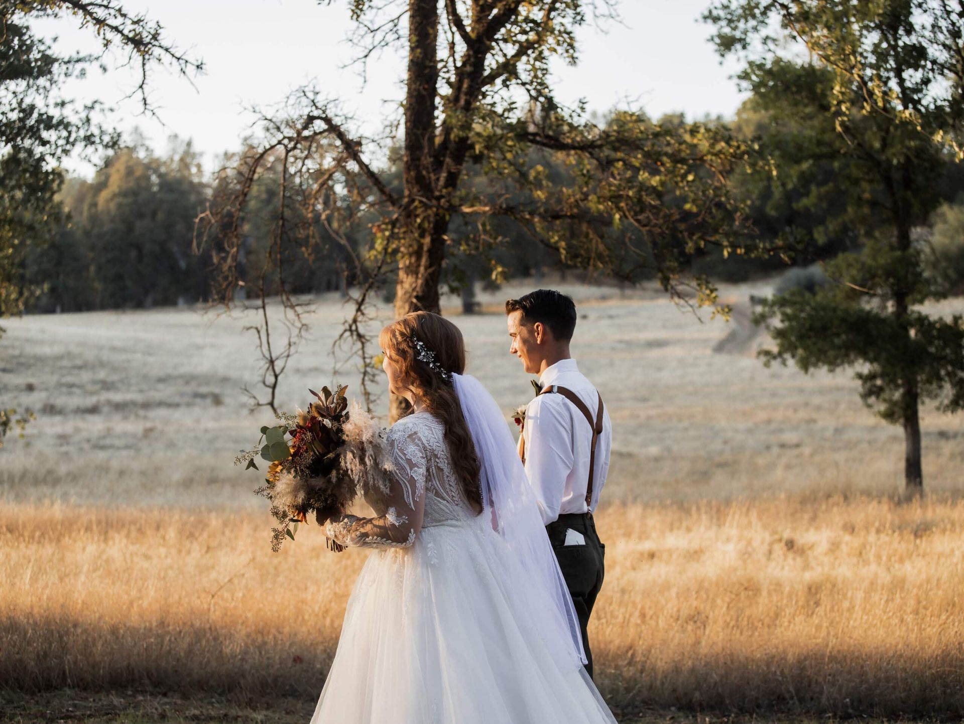 A bride and groom are standing in a field with trees in the background.